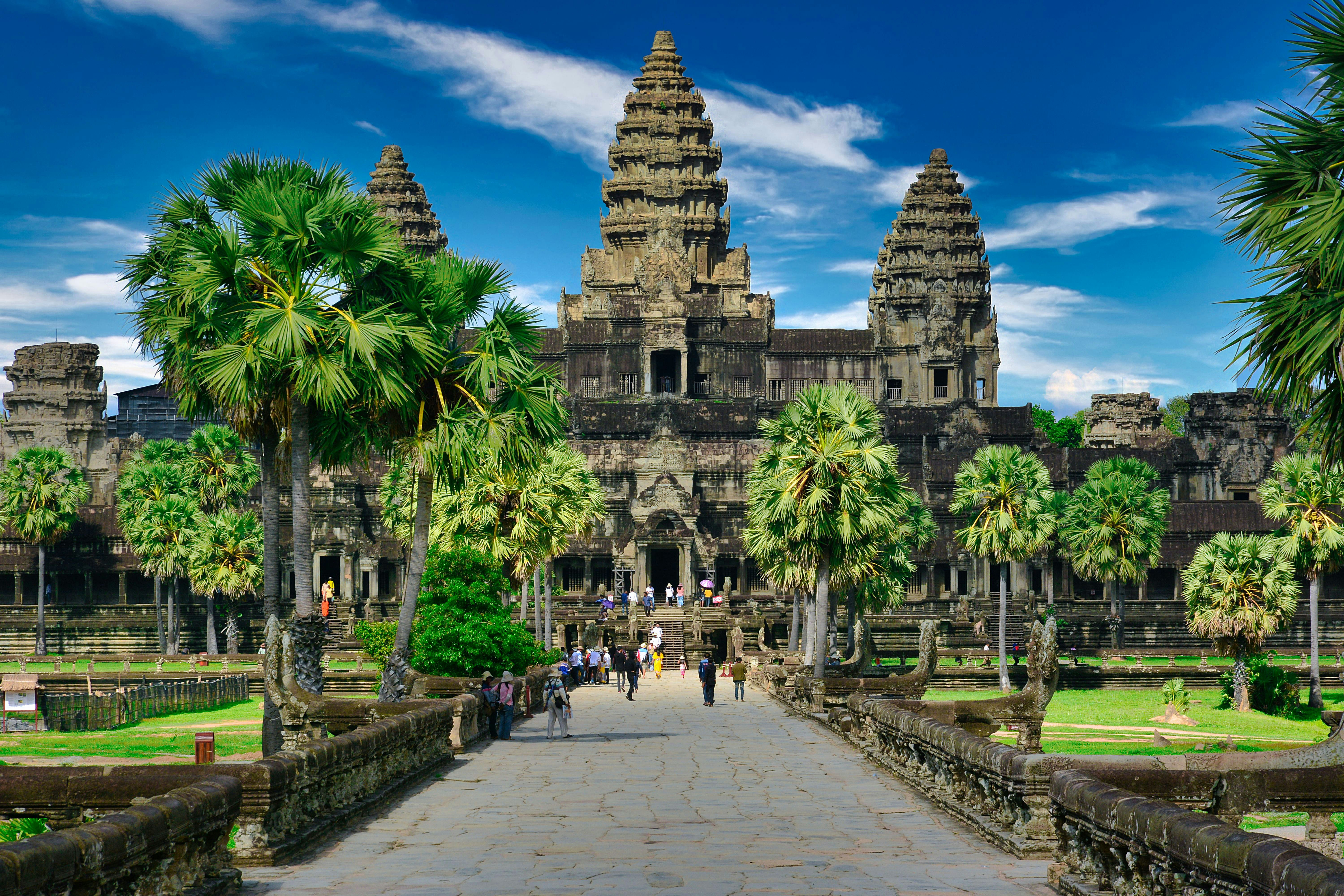 A stone temple with trees and people walking down a paved pathway